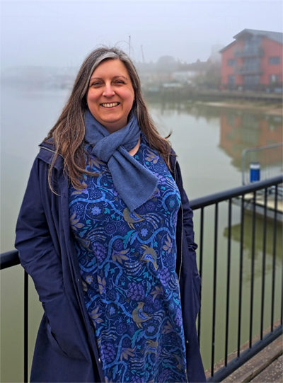 A picture of a woman smiling, standing on Wivenhoe's river jetty, in the morning mist
